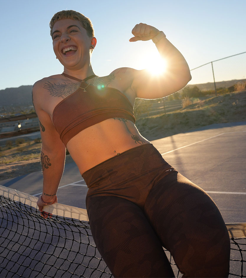 The coach laughs and flexes on an outdoor court at sunset.